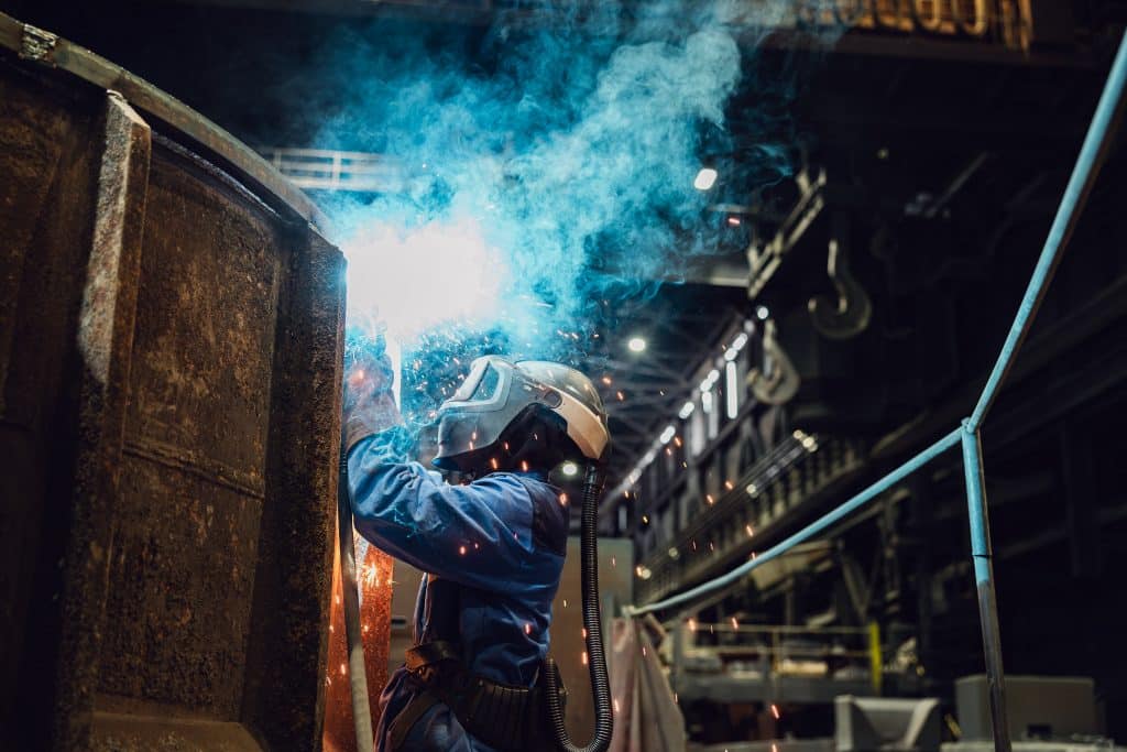 Schweisser mit Schutzhelm arbeitet an grossem Stahlbehaelter in Industriehalle in Oberhausen