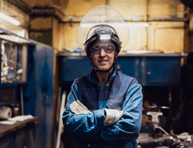Mitarbeiter mit Schutzhelm und verschraenkten Armen in Werkstatt