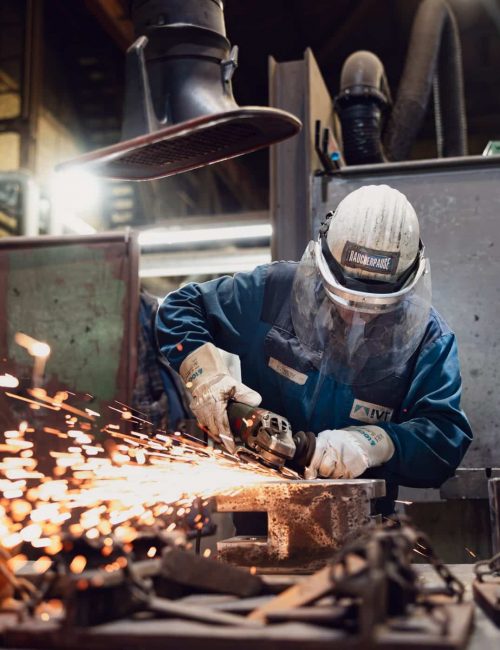 Mitarbeiter mit Schutzhelm schleift Metall und Funken spruehen
