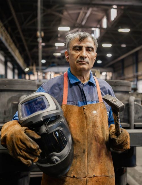 Aelterer Mitarbeiter haelt Schweisshelm in Produktionshalle