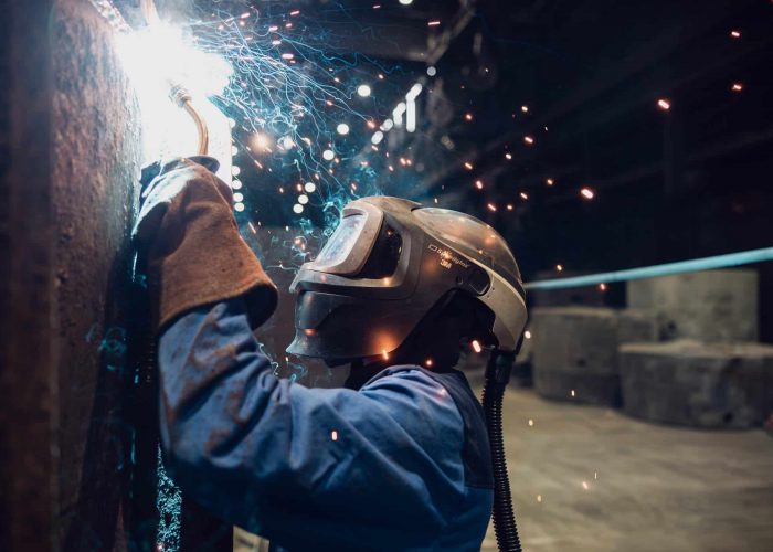 Schweisser mit Visier arbeitet an Metall mit hellen Funken