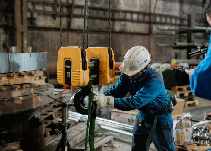 Mitarbeiter mit Schutzhelm befestigt Last mit Hebegurt