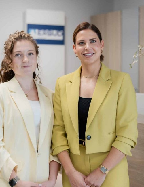 Zwei Mitarbeiterinnen im Bueroeingang laecheln in die Kamera